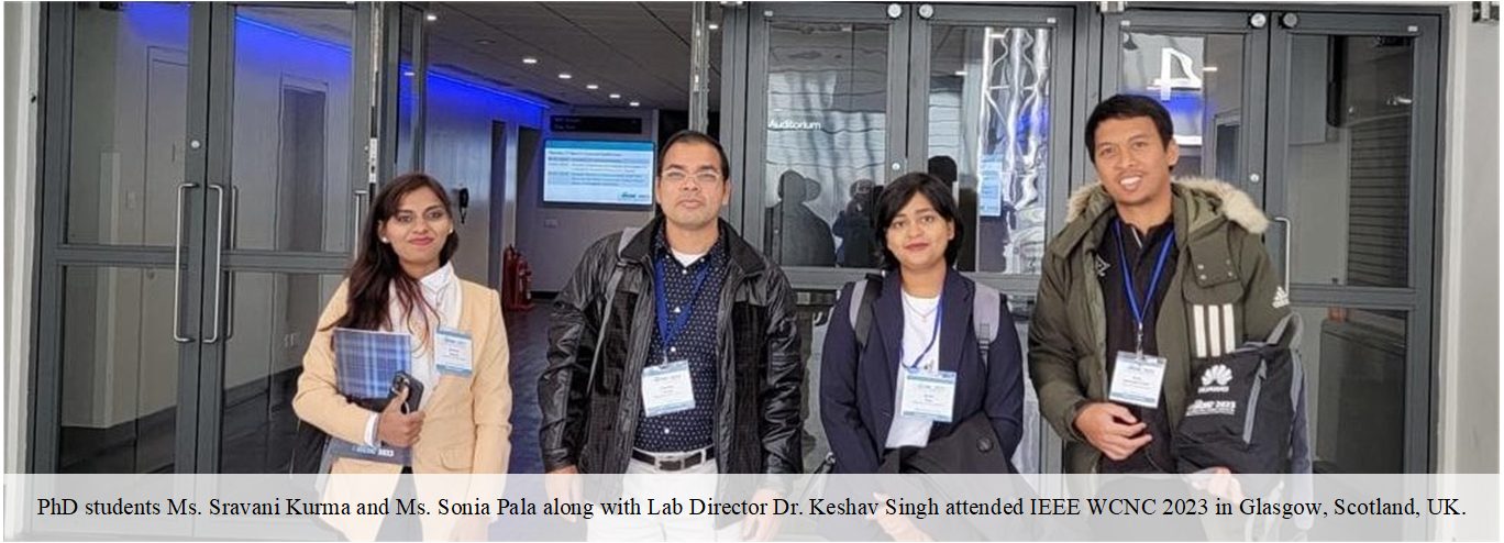 Four people with conference badges standing at the entrance of the IEEE WCNC 2023 venue in Glasgow.