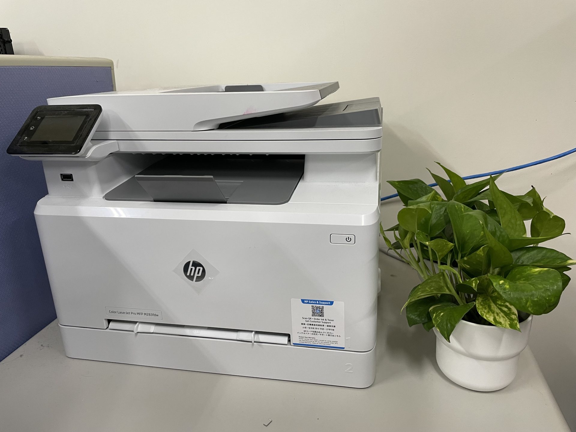 A colour laser multifunction printer on a lab desk next to a potted plant