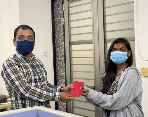 Reward presentation: a lab member wearing a face mask and grey jacket receives a red envelope.