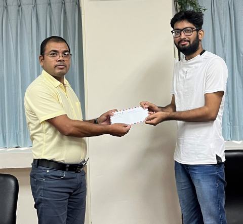 Reward presentation in the lab office: a lab member in a white T-shirt receives an envelope.