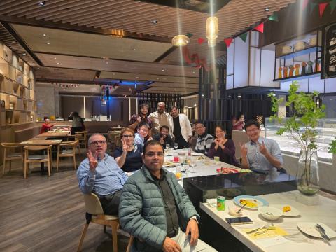 Speakers and hosts smile and make peace signs around a restaurant table decorated for Christmas.