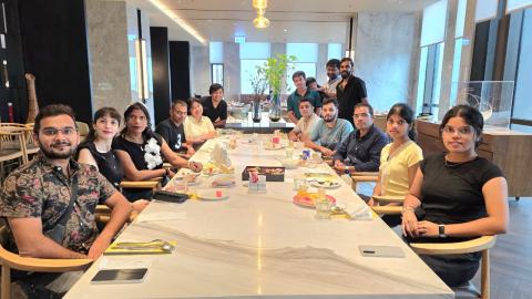 Lab members and family seated around a long restaurant table set with drinks, smiling at the camera.