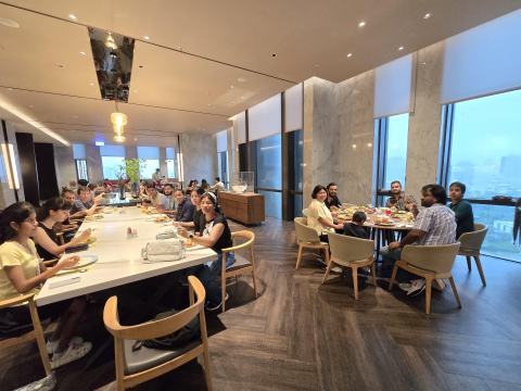 Lab members eating at a long table and a round table in a restaurant with large windows overlooking the city.