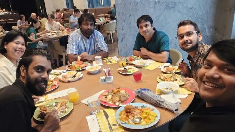 Selfie of six lab members smiling around a round restaurant table with plates of food and drinks.