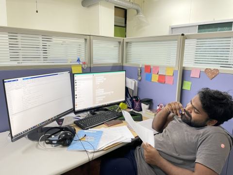 A lab member reading printed papers at a workstation with two monitors.
